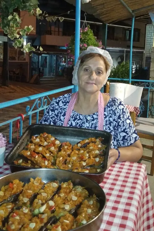 The cook on the terrace holding a tray of freshly baked stuffed eggplants