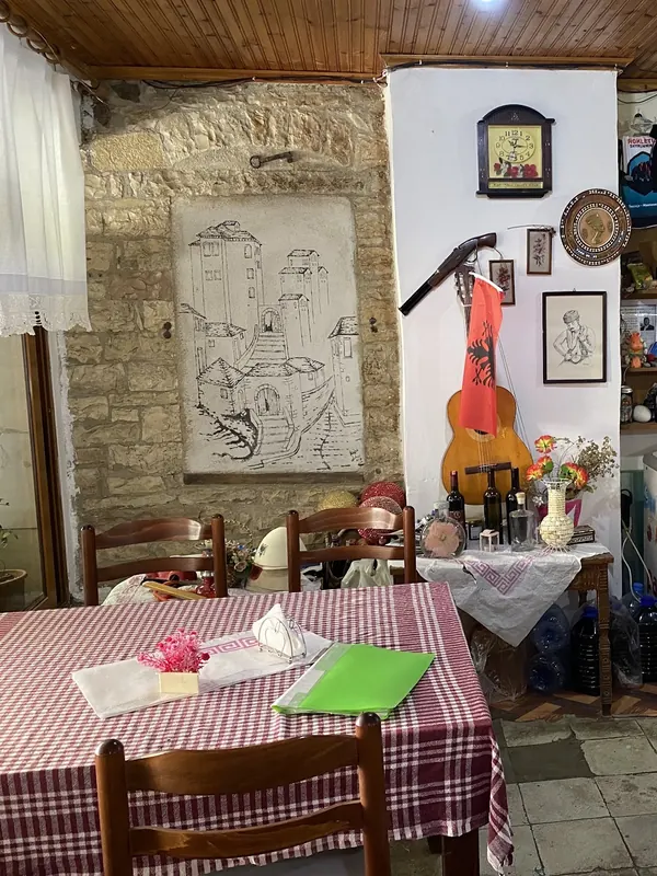 Inside the taverna: a drawing of old Gjirokastër on the stone wall, a guitar and checked tablecloths