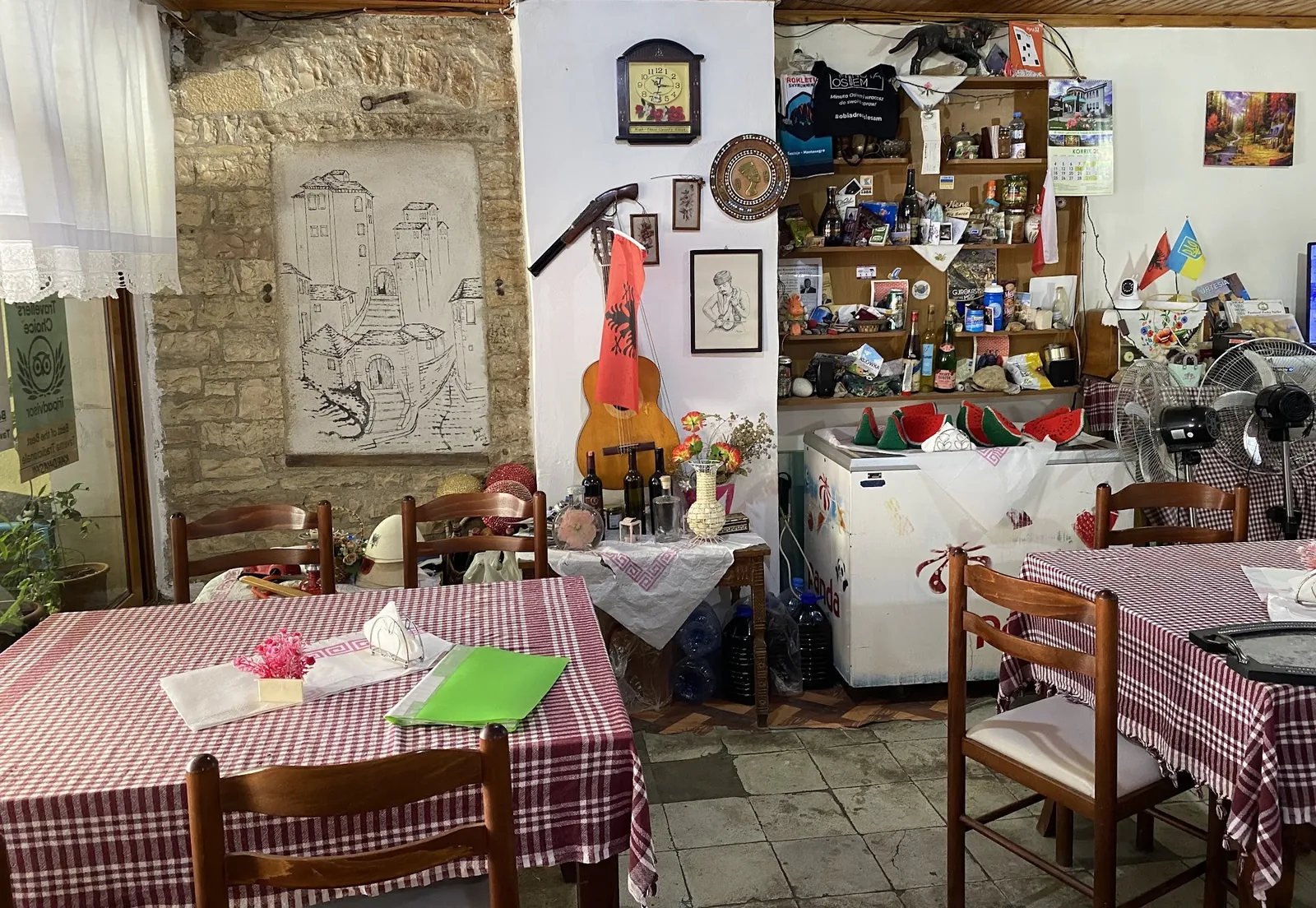 The dining room: a drawing of old Gjirokastër on the stone wall, a guitar and checked tablecloths