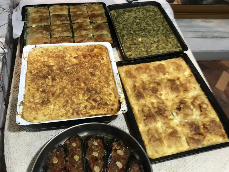 Trays of spinach pie, cheese pie and moussaka next to a pan of stuffed eggplants